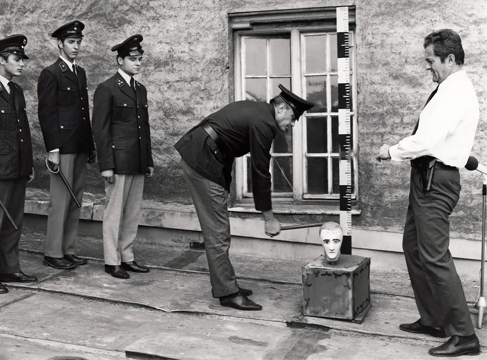 Standfoto für - Nicht fummeln Liebling ! - mit Hans Fries als Polizei-Ausbilder bei einem fiktiven Schlagstock-Training von einer Reihe von Polizisten an einem Hau-den- Lukas, die dadurch grotesk ihre Schlagkraft mit dem Gummiknüppel trainieren, indem sie auf einen Lukas-Kopf schlagen sollen