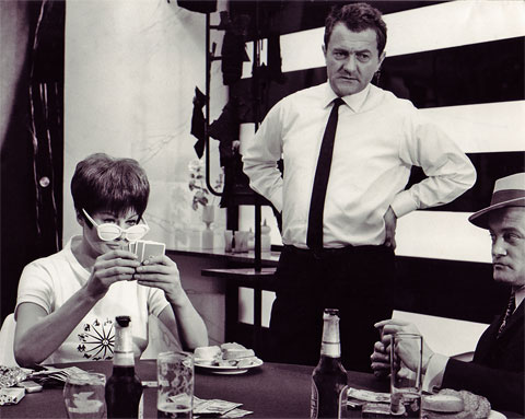 Standfoto für den Spielfilm „Das gewisse Etwas der Frauen“ und einer Szene am Spieltisch mit einer Schauspielerin und einem Schauspieler, in der Mitte stehend Produktionsleiter Hans Fries