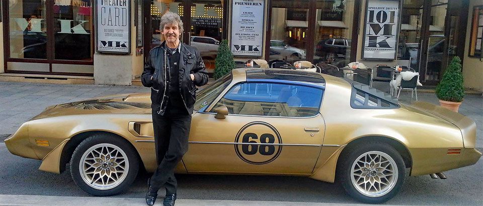 Fotograf Mike Gallus vor einem goldenen Pontiac Trans Am in der Münchner Innenstadt